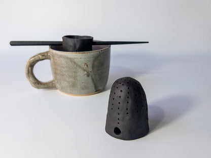 Ceramic mug with a black tea strainer on a white background