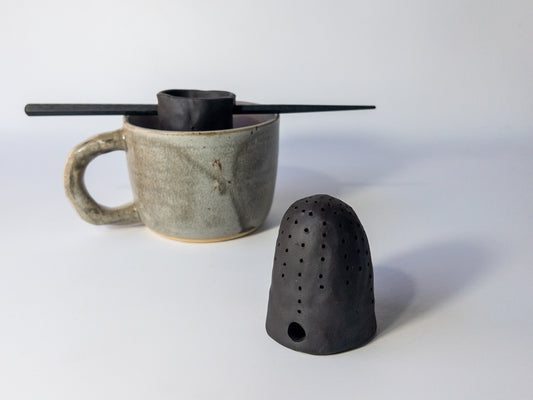 Ceramic mug with a black tea strainer on a white background