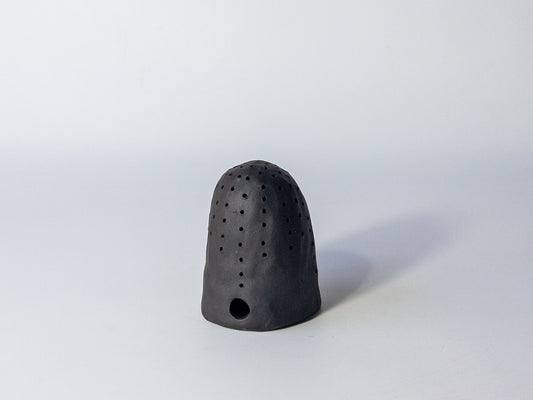 Black ceramic tea strainer with holes on a white background
